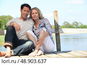mid age couple seated on a pontoon near a lake. Стоковое фото, агентство Ingram Publishing / Фотобанк Лори