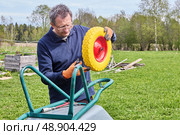 Replacing old wheel with solid polyurethane wheel on garden wheelbarrow to ensure smooth movement and prevent future punctures. Стоковое фото, фотограф Владимир Григорьев / Фотобанк Лори