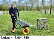Solid polyurethane wheel recently installed is being inspected as gardener pushes garden wheelbarrow forward while slightly tilting to monitor new wheel performance. Стоковое фото, фотограф Владимир Григорьев / Фотобанк Лори