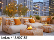 Cozy outdoor lounge area featuring stylish seating with cushions, decorative poufs, and ambient lighting, surrounded by greenery and modern architecture, perfect for relaxation and social gatherings. Стоковое AI-изображение, AI-художник Ирина Ручушкина / Фотобанк Лори