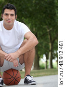 Man crouching on basketball. Стоковое фото, агентство Ingram Publishing / Фотобанк Лори