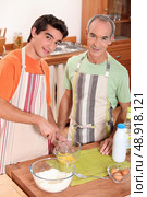 a young man and his grand father wearing aprons and making a cake. Стоковое фото, агентство Ingram Publishing / Фотобанк Лори