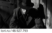 A man in a fedora leans against a wooden doorway, his face obscured by shadows. Стоковое AI-изображение, AI-художник Данила Большаков / Фотобанк Лори