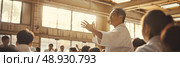 A karate instructor, wearing a white gi, demonstrates a technique to his students in a Japanese dojo. The students are attentively watching as the instructor performs the move with precision. Стоковое AI-изображение, AI-художник Данила Большаков / Фотобанк Лори