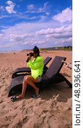 A girl takes pictures of the sea sitting on a chaise longue on the beach on a cool day. Стоковое фото, фотограф K. / Фотобанк Лори