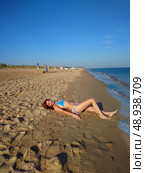 A young woman in a blue swimming suit is lying on a sandy beach near the sea on a clear day. Редакционное фото, фотограф K. / Фотобанк Лори