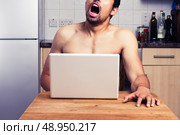 Young man is watching pornography on his laptop in the kitchen. Стоковое фото, агентство Ingram Publishing / Фотобанк Лори