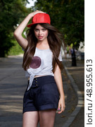 beautiful long haired teen model on pave. red cap, grey t-shirt, dark blue shorts. Стоковое фото, агентство Ingram Publishing / Фотобанк Лори