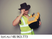 A cowboy builder with a big tool box is pulling silly faces and gesturing. Стоковое фото, агентство Ingram Publishing / Фотобанк Лори