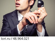 Businessman is covering the phone to speak in private to someone in the room. Стоковое фото, агентство Ingram Publishing / Фотобанк Лори