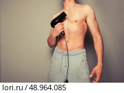 Athletic young man is holding a hair dryer and messing around with it. Стоковое фото, агентство Ingram Publishing / Фотобанк Лори