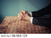 Man in suit with his hands folded in prayer at a desk with light streaming through blinds. Стоковое фото, агентство Ingram Publishing / Фотобанк Лори
