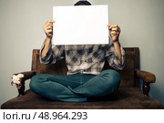 man on sofa holding a sign. Стоковое фото, агентство Ingram Publishing / Фотобанк Лори