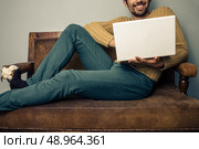Happy young man lying on sofa is working on laptop. Стоковое фото, агентство Ingram Publishing / Фотобанк Лори