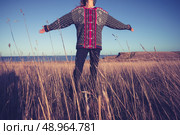 Woman with her arms raised in a field by the sea at sunset. Стоковое фото, агентство Ingram Publishing / Фотобанк Лори