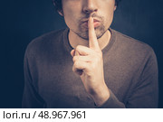 Young man is signalling hush with his finger on his lips. Стоковое фото, агентство Ingram Publishing / Фотобанк Лори