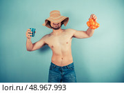 A young shirtless man wearing a large beach hat is holding a net of clementines. Стоковое фото, агентство Ingram Publishing / Фотобанк Лори
