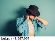 A sexy young cowboy is standing by a blue wall with his shirt unbuttoned. Стоковое фото, агентство Ingram Publishing / Фотобанк Лори