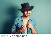 A sexy young cowboy is standing by a blue wall with his shirt unbuttoned. Стоковое фото, агентство Ingram Publishing / Фотобанк Лори