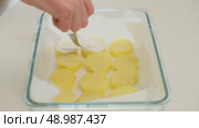 Close-up of a hand adding cream on sliced boiled potatoes in a glass baking dish lined with parchment paper. Стоковое видео, видеограф Андрей Журавлев / Фотобанк Лори