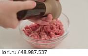 Person seasons raw ground meat with black pepper from a pepper shaker, preparing ingredients for a homemade dish in the kitchen. Стоковое видео, видеограф Андрей Журавлев / Фотобанк Лори