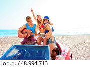 young group having fun on the beach playing guitar and dancing in a convertible car. Стоковое фото, агентство Ingram Publishing / Фотобанк Лори