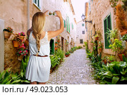 Blond tourist girl taking photos of Mallorca Valldemossa village street photomount. Стоковое фото, агентство Ingram Publishing / Фотобанк Лори