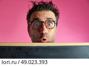Nerd man crazy behind a blackboard funny surprise gesture in pink background. Стоковое фото, агентство Ingram Publishing / Фотобанк Лори