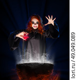 Young witch with red potion on blue rays background. Стоковое фото, агентство Ingram Publishing / Фотобанк Лори