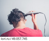 A young man is using hair clippers to give himself a haircut. Стоковое фото, агентство Ingram Publishing / Фотобанк Лори