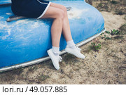 A young woman wearing a blue dress is sitting on an upturned boat on the beach. Стоковое фото, агентство Ingram Publishing / Фотобанк Лори