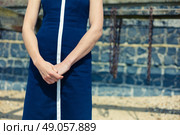 A young woman wearing a blue dress is standing on the beach on a sunny day by an old wooden structure with rusty chains hanging from it. Стоковое фото, агентство Ingram Publishing / Фотобанк Лори