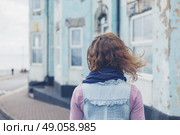 A young woman is standing in the street outside a blue house by the coast on a windy day. Стоковое фото, агентство Ingram Publishing / Фотобанк Лори