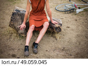 A young woman with bruises on her leg is sitting on a log outside, there is a bicycle in the background. Стоковое фото, агентство Ingram Publishing / Фотобанк Лори
