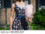 A young woman wearing a dress is standing outside an old farmhouse with a candyfloss on a sunny summer day. Стоковое фото, агентство Ingram Publishing / Фотобанк Лори