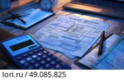 Bue calculator rests on wooden desk with a tax form and other paperwork nearby. image captures the essentials for calculating taxes and highlights the need for careful financial planning. Стоковое AI-изображение, AI-художник Данила Большаков / Фотобанк Лори