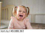 Little Girl joking sticking tongue out with silly expression. Child making face. Funny foolishness portrait of baby girl laughing in bedroom. Adorable Caucasian kid doing crazy comical gesture at home. Стоковое фото, фотограф Марина Демидюк / Фотобанк Лори