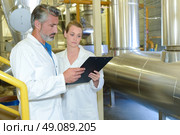 Man and woman looking at clipboard, stood next to metal vat. Стоковое фото, агентство Ingram Publishing / Фотобанк Лори
