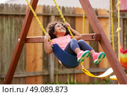 Kid toddler girl swinging on a playground swing in the backyard latin ethnicity. Стоковое фото, агентство Ingram Publishing / Фотобанк Лори