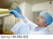 Factory worker refilling hopper of lids in machine. Стоковое фото, агентство Ingram Publishing / Фотобанк Лори