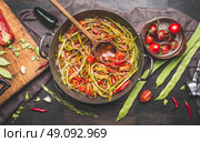 Green French beans meal preparation with wooden spoon. Green French beans in cooking pot with tomatoes sauce and ingredients on dark rustic background, top view.  Vegetarian food concept. Стоковое фото, агентство Ingram Publishing / Фотобанк Лори