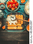 Strawberry tiramisu making. Dish with cookies, creme and spoon on rustic kitchen table with tiramisu cooking ingredients, top view, place for text. Italian food concept. Стоковое фото, агентство Ingram Publishing / Фотобанк Лори