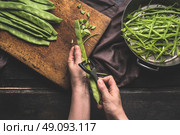 Green french beans,  preparation on dark kitchen table. Woman Female hands cut beans with vegetable peeler. Cutting board with Green french beans and sliced beans , top view. Стоковое фото, агентство Ingram Publishing / Фотобанк Лори