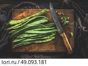 Green french beans on rustic cutting board with kitchen knife on dark wooden background, top view.  Legumes vegetables. Стоковое фото, агентство Ingram Publishing / Фотобанк Лори