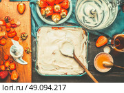 Strawberry tiramisu cake making with cake dish , wooden spoon and mascarpone cream on dark  rustic background, top view. Italian food concept. Стоковое фото, агентство Ingram Publishing / Фотобанк Лори