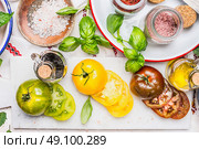 Sliced colorful tomatoes assortment on marble cutting board on light kitchen table with ingredients in enamelled bowls. Summer food concept. Стоковое фото, агентство Ingram Publishing / Фотобанк Лори