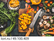 Chopped Pumpkin on rustic cutting board with kitchen knife and mushrooms and vegetables ingredients  for tasty vegetarian cooking, dark styled,  top view. Стоковое фото, агентство Ingram Publishing / Фотобанк Лори