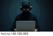 Мужчина в маске балаклаве и с гарнитурой за ноутбуком. Стоковое AI-изображение, AI-художник Илья Старков / Фотобанк Лори