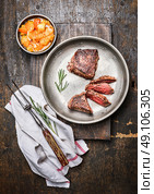 Sliced medium rare roasted beef steak, filet mignon , in metal rustic plate with meat fork and salsa sauce on dark wooden background, top view. Стоковое фото, агентство Ingram Publishing / Фотобанк Лори
