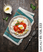 Chicken tomato stew with basmati rice with yoghurt sauce in plate and fork on wooden background, top view. Стоковое фото, агентство Ingram Publishing / Фотобанк Лори